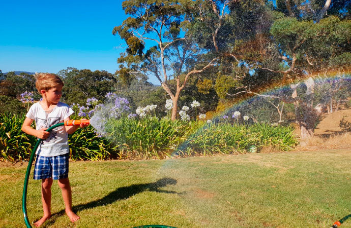 Niño haciendo un arco iris con agua y una manguera